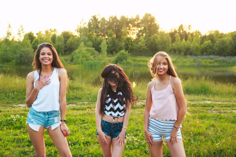 Three Beautiful Girls Walking And Laughing On Sunset In The Park