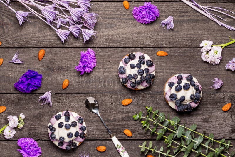 Three blueberry Graham Cheesecakes topped with fresh berries with a spoon on a dark wood background with almonds, purple flowers royalty free stock photography Three blueberry Graham Cheesecakes topped with fresh berries with a spoon on a dark wood background with almonds, purple flowers royalty free stock photography