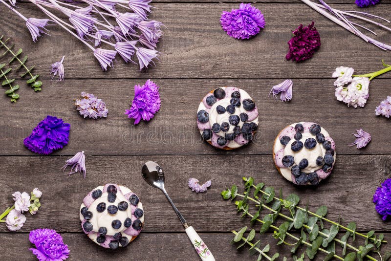 Three blueberry Graham Cheesecakes topped with fresh berries with a spoon on a dark wood background with purple flowers and twigs stock photo Three blueberry Graham Cheesecakes topped with fresh berries with a spoon on a dark wood background with purple flowers and twigs stock photo