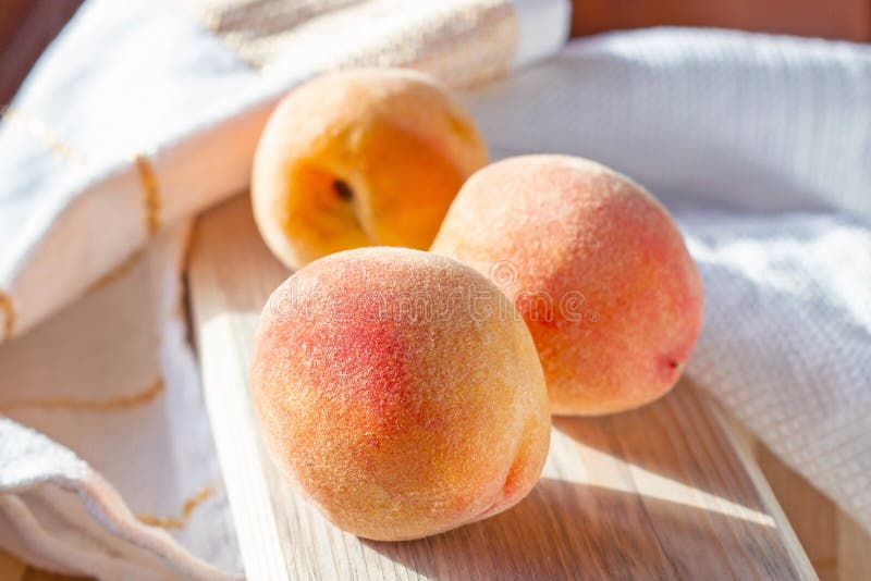Three bright fresh juicy red and orange peaches on the wooden board in the sunny kitchen in summer. royalty free stock photos Three bright fresh juicy red and orange peaches on the wooden board in the sunny kitchen in summer. royalty free stock photos