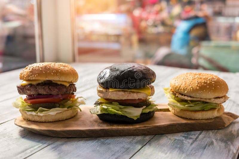 Three burgers on wood board.