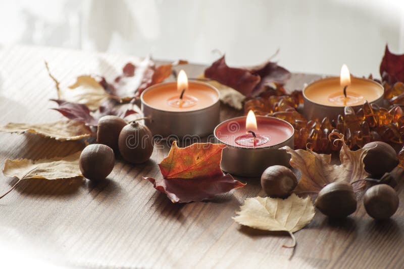 Three burning candles, colorful autumn leaves and acorns of northern red oak and amber necklace