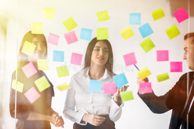 Three businesspeople discussing and planning concept. Front of glass wall marker and stickers. Startup office. royalty free stock photos Three businesspeople discussing and planning concept. Front of glass wall marker and stickers. Startup office. royalty free stock photos
