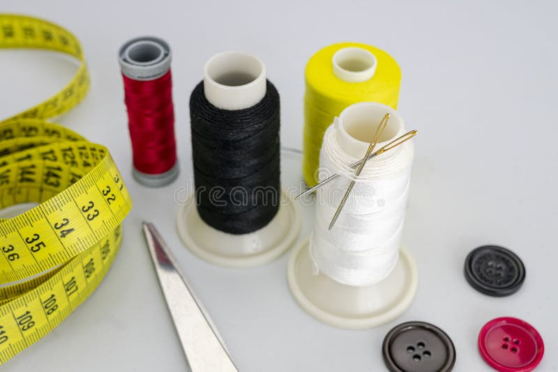 Three buttons, colored sewing thread bobbins with two needles, scissors and a seamstress tape measure