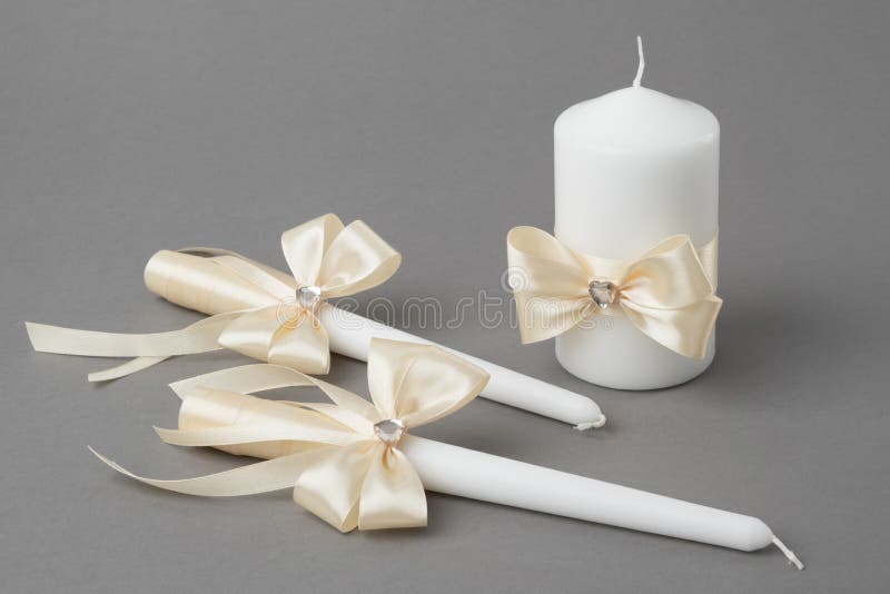 Three candles decorated with beige silk bows on gray background. stock photo