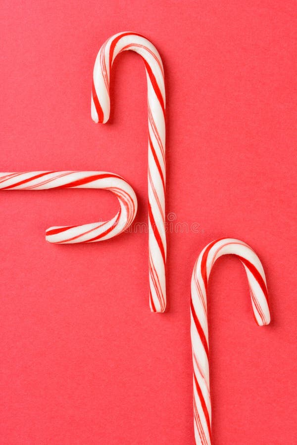 High angle shot of three Christmas candy canes on a red background. The peppermint sticks run in different directions and out of the frame. Vertical format with copy space. High angle shot of three Christmas candy canes on a red background. The peppermint sticks run in different directions and out of the frame. Vertical format with copy space.