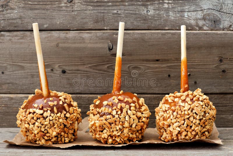 Three caramel apples with nuts against rustic wood royalty free stock photo
