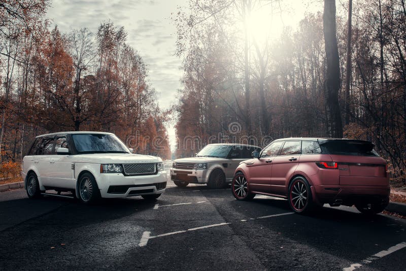 Three cars Land Rover Range Rover parked at autumn forest asphalt road at sunny daytime