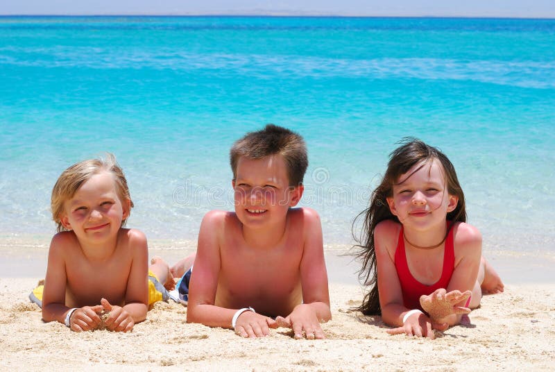 Tre bambini sono sdraiati su una spiaggia tropicale.