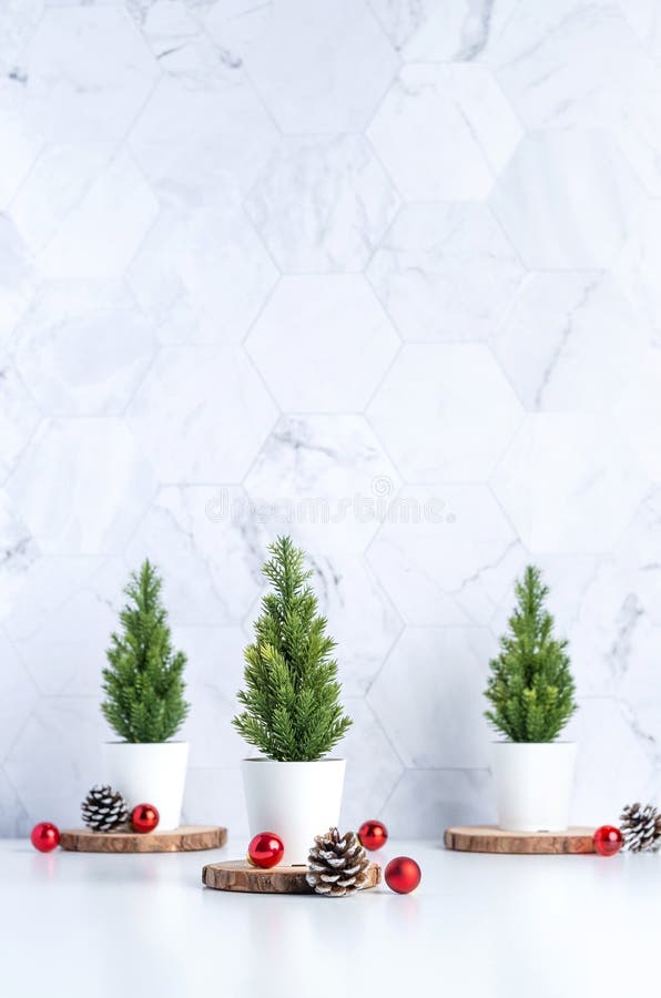 Three christmas tree with pine cone and decor xmas ball on white table and marble tile wall background.clean minimal simple style.