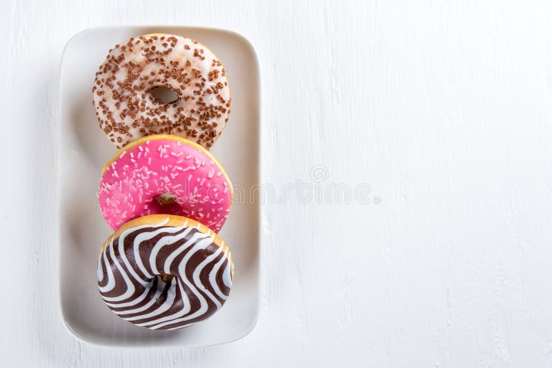 Three colorful donut on a plate on a white table royalty free stock photography