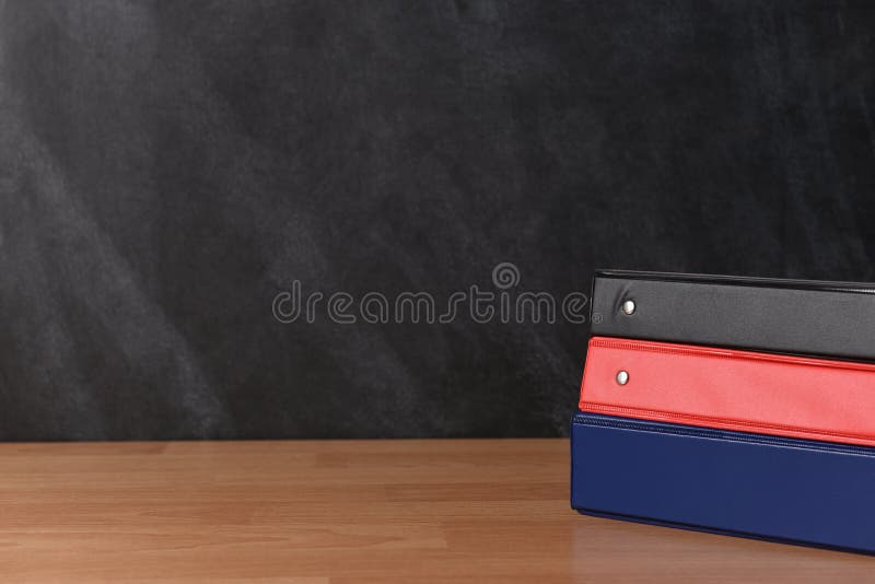 Three different binders laying on a teachers desk in front of a chalk board
