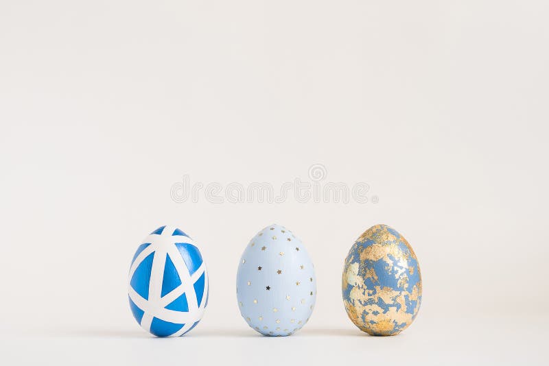 Three Easter golden decorated eggs on blue background. Minimal easter concept. Happy Easter card with copy space for