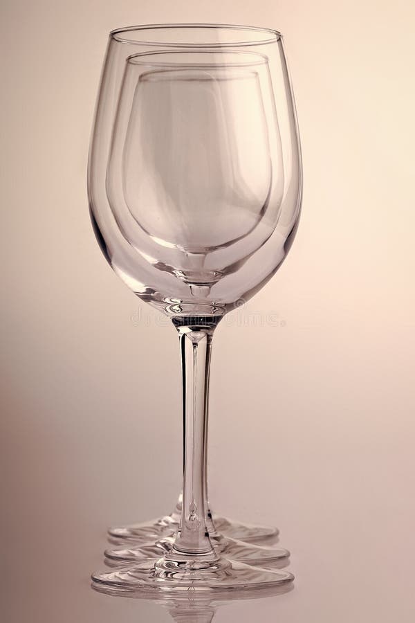 Closeup of three transparent clear crystal empty wine glasses standing close to each other in row on chromium white and grey background, vertical picture. Closeup of three transparent clear crystal empty wine glasses standing close to each other in row on chromium white and grey background, vertical picture