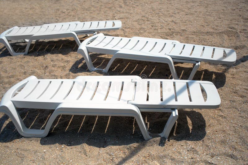 Three Empty White Plastic Deck Chairs Chaise Lounges at Sandy Beach during Sunny Day Top View