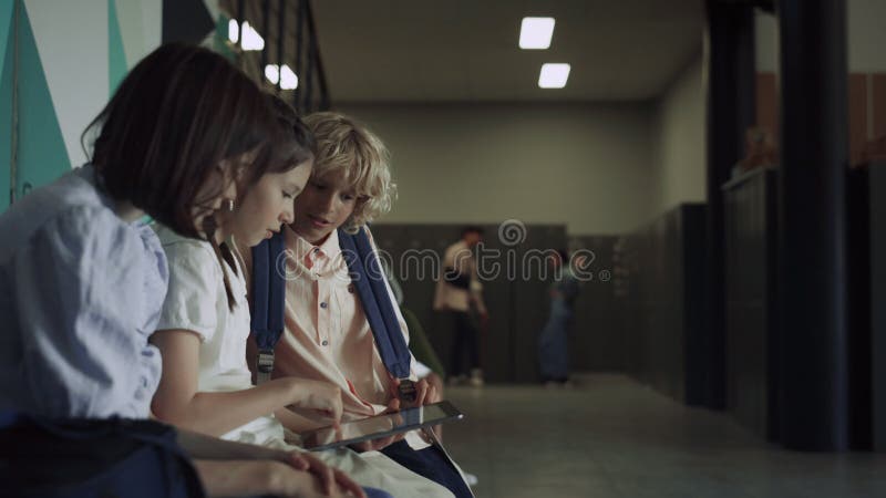 Three focused students sitting with tablet in school hall. Preteen communication stock video footage