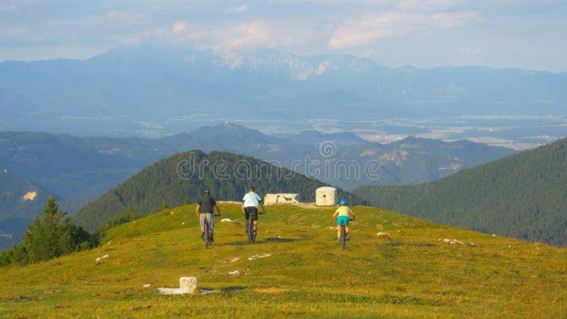 Three friends racing on their bicycles down a steep grassy hill on a sunny day. royalty free stock photography
