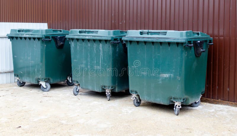 Three green trash cans are lined up against a brown wall stock image