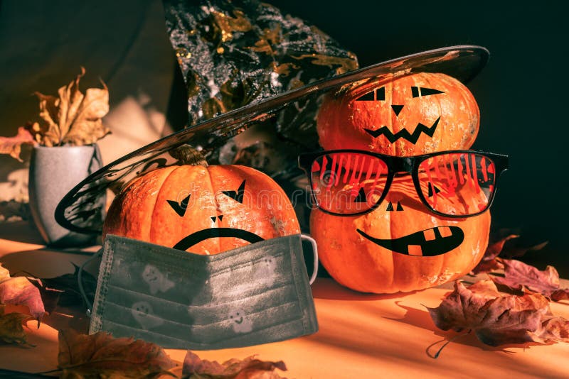 Three halloween pumpkins painted as Jack`s lantern in festive bloody glasses, hat, face mask with leaves and shadows royalty free stock photos