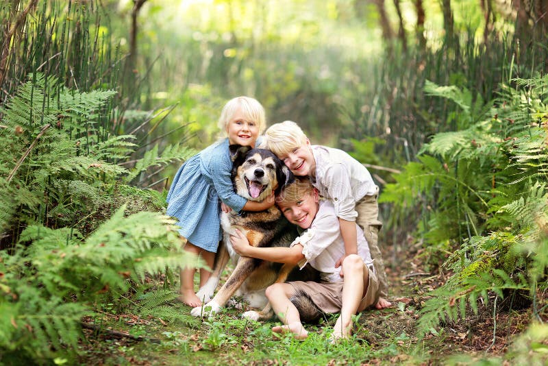 Three Happy Children Lovinglt Hugging the Pet Dog in the Forest