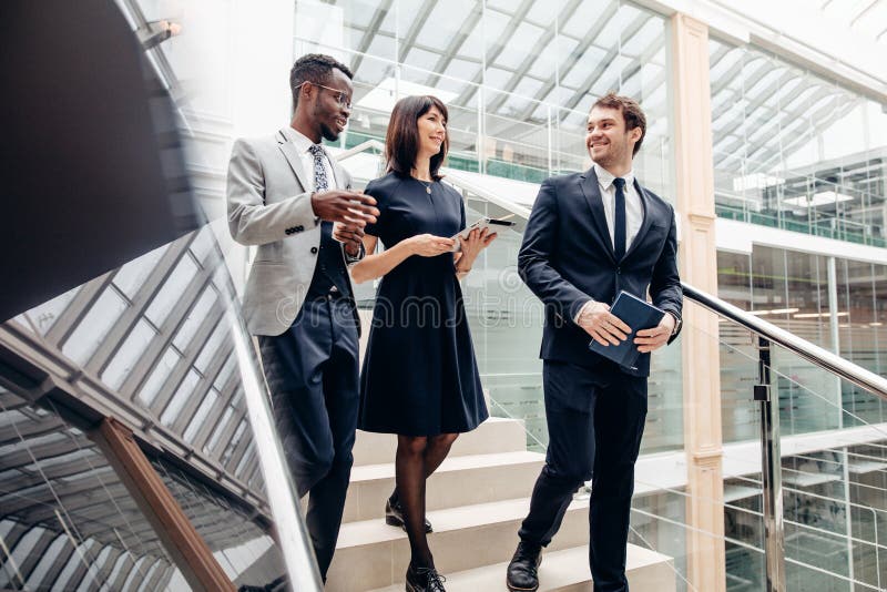 Three multiracial business people walking down on stairs with digital tablet royalty free stock photography Three multiracial business people walking down on stairs with digital tablet royalty free stock photography