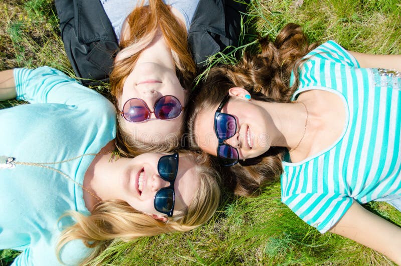 Three happy smiling girls lying on green grass in sunglasses