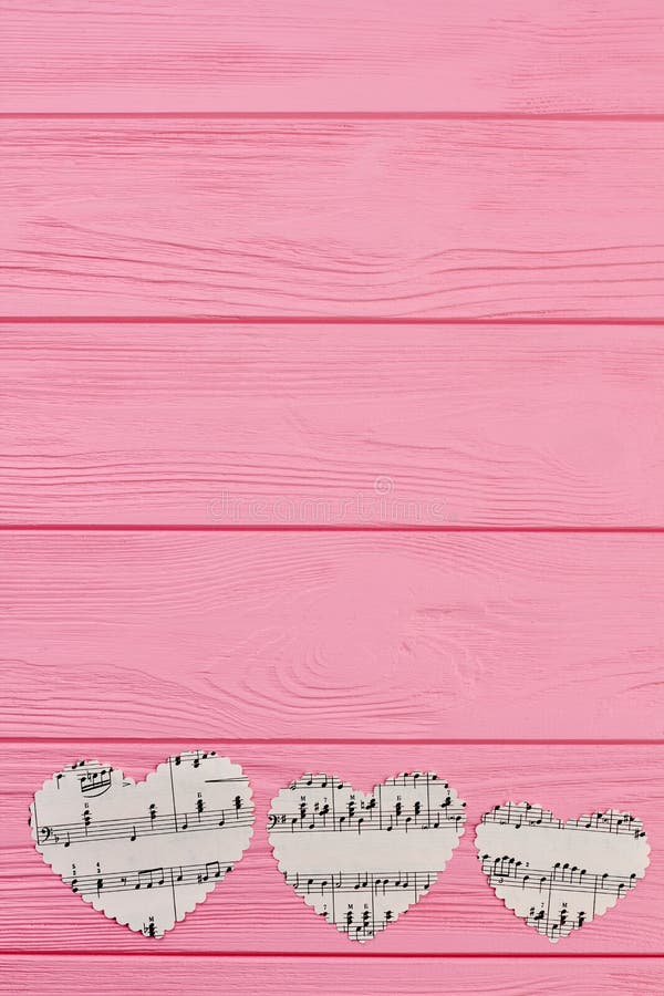 Three hearts with music notes. Row of paper heart shaped cutouts with musical notes on pink wooden background, copy space.