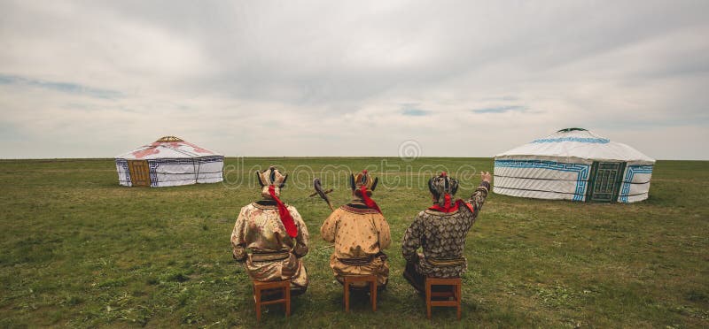 Three Kalmyk musicians in national costumes in the steppe against the background of yurts, the spring steppe