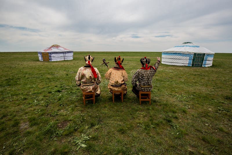 Three Kalmyk musicians in national costumes in the steppe against the background of yurts, the spring steppe