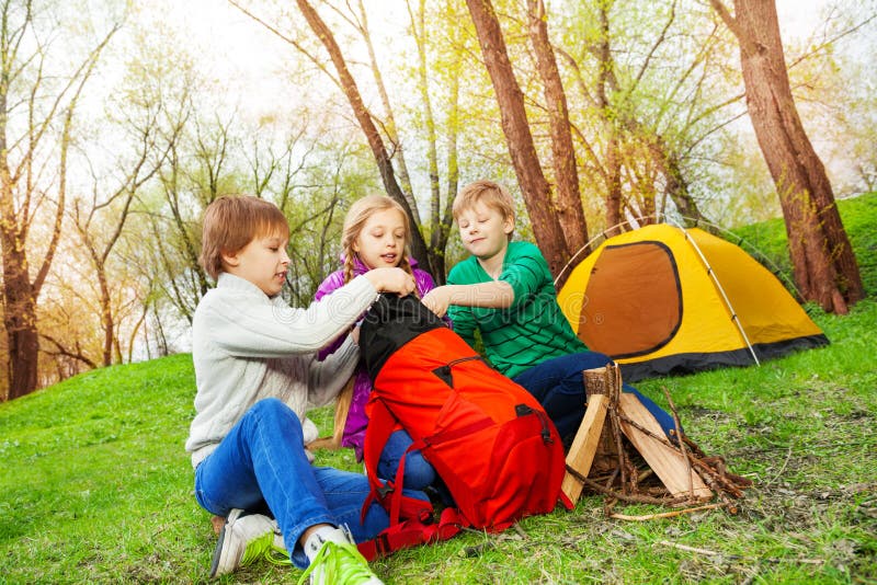 Three kids packing the things into red rucksack