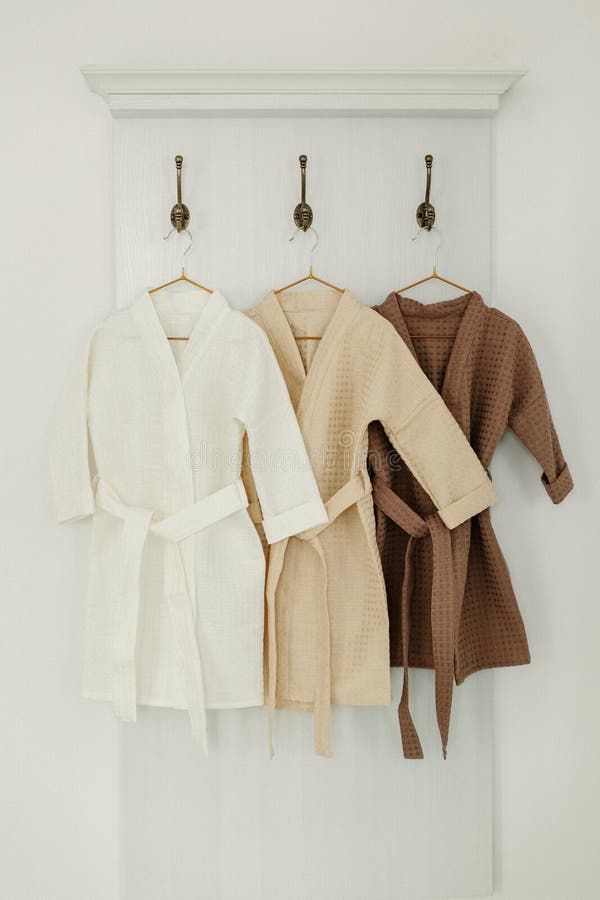 Three Linen Robes of Different Colors Hang on a Hanger in the Bathroom