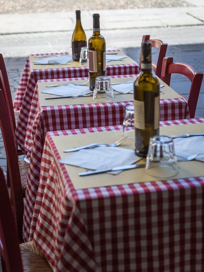 Three Little Wooden Tables Set with Red Checked Tablecloth, Wine Bottles and Cutlery.