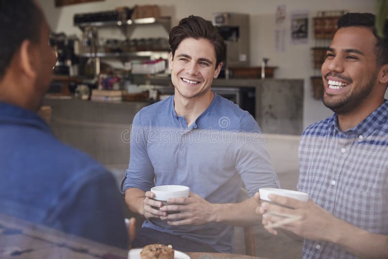 Three Male Friends Laughing Over Coffee at a Coffee Shop Stock Image