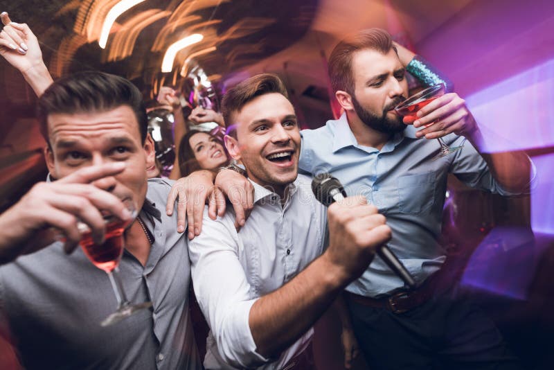 Three men sing at a karaoke club. Young people have fun in a nightclub. They are very cheerful and they smile.