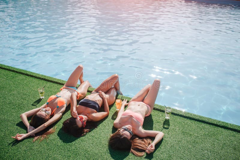 Three models are lying on grass. They holds legs in water and get tan from sun. Models stratching and sleeping. They are stock photos Three models are lying on grass. They holds legs in water and get tan from sun. Models stratching and sleeping. They are stock photos