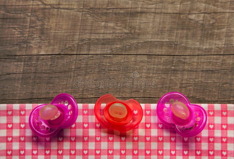 Three pacifier or comforter on wooden checked pink white fabric