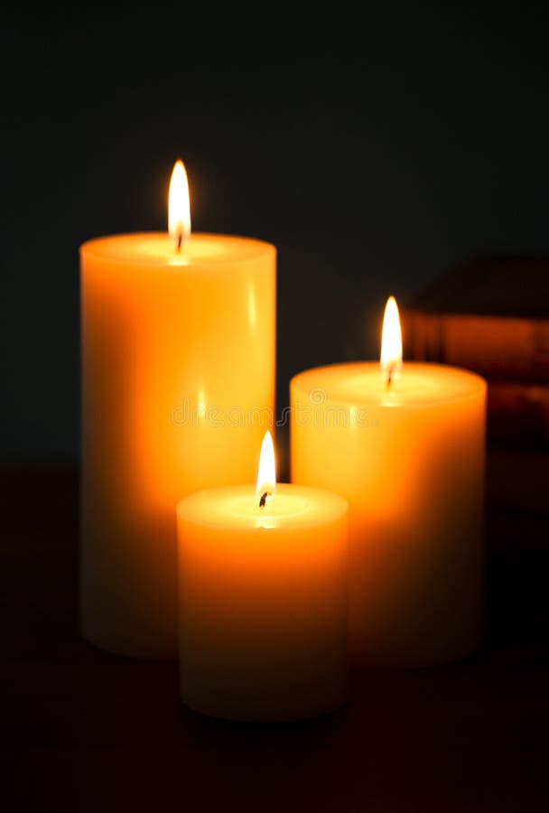 Three Pillar Candles Burning in a Dark Room with a Stack of Antique