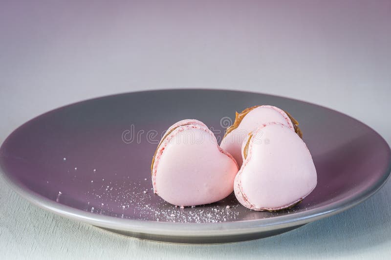 Three pink hearts on a plate. Sweet pastel french macaroons on light table.