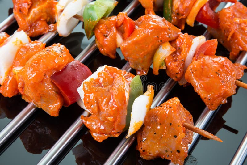 Three raw shaslik skewers on a cooking grate with reflections on