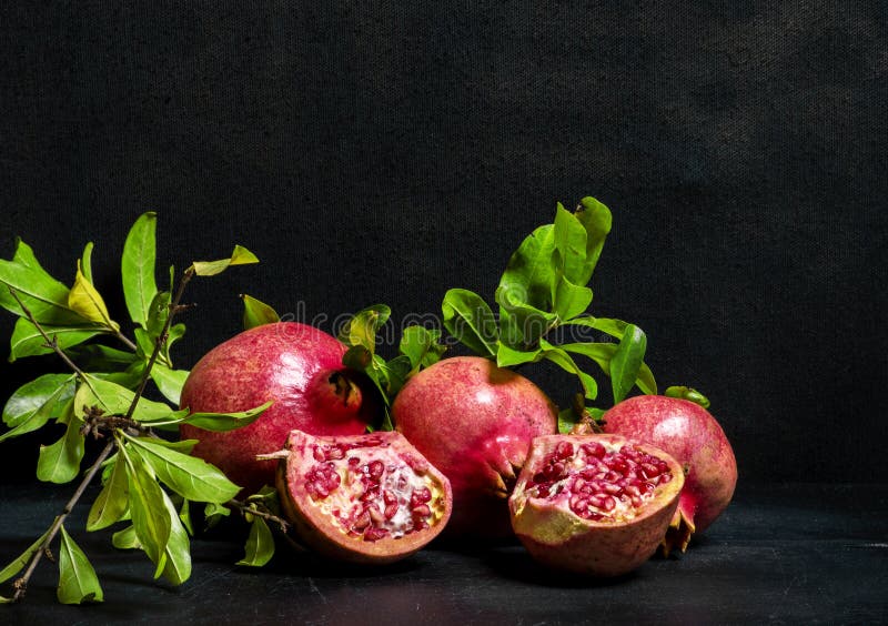 Three red pomegranates and one pomegranade cut in half with green leafs