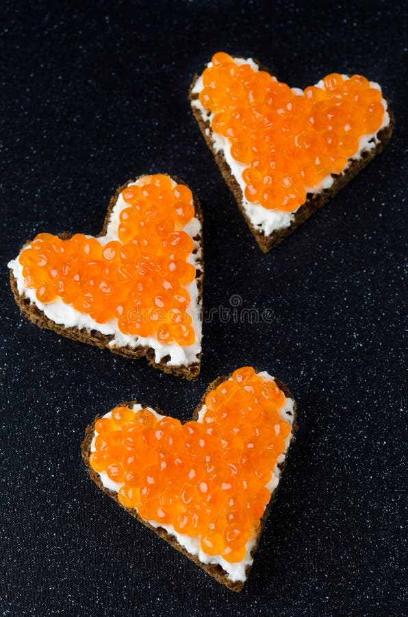Three sandwich with red caviar in the form of a heart on a black