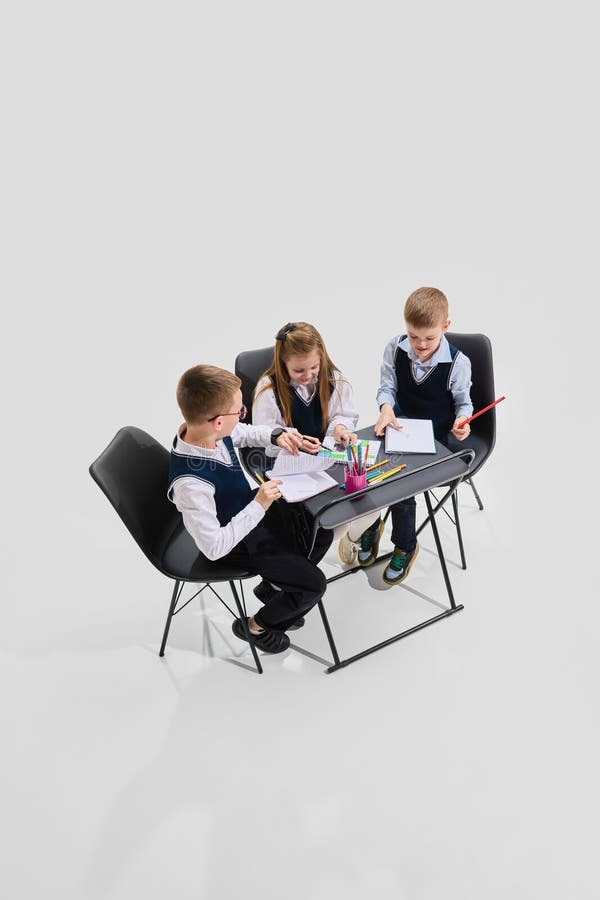 Three schoolchildren in uniform working together at shared desk with open notebooks and pencils, engaging in creative group study. royalty free stock image