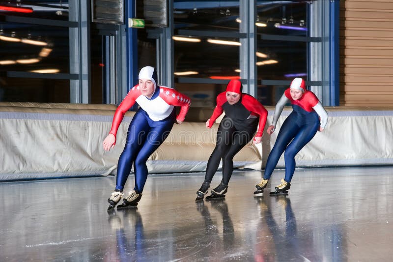 Three speed skaters making their laps on an indoor ice rink