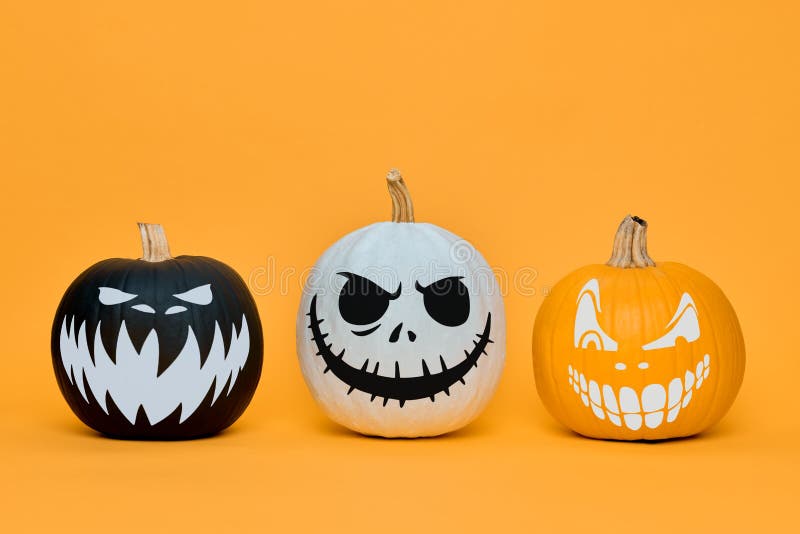 Three Spooky Halloween Pumpkins with Scary Face Expressions Over Orange ...
