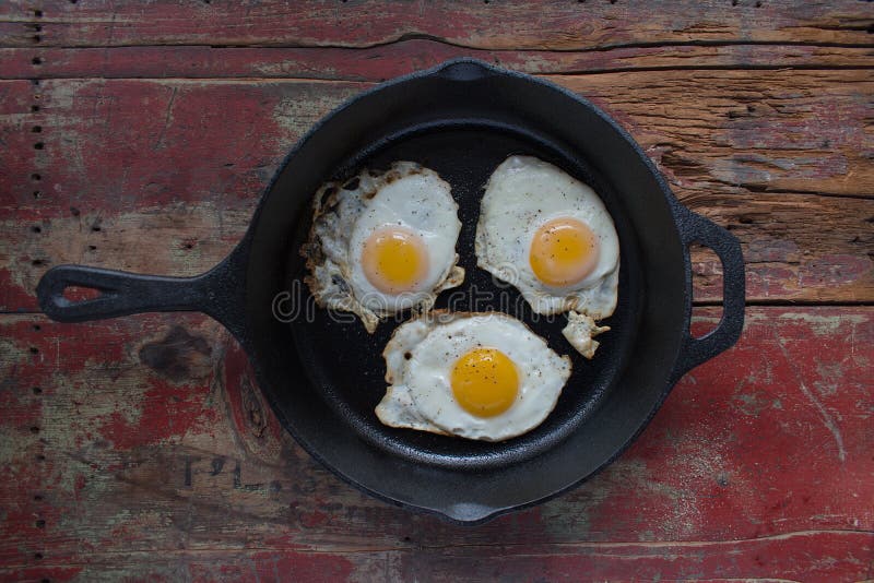 Three Sunny Side Up Fried Eggs in Cast Iron Pan on Wooden Table Stock