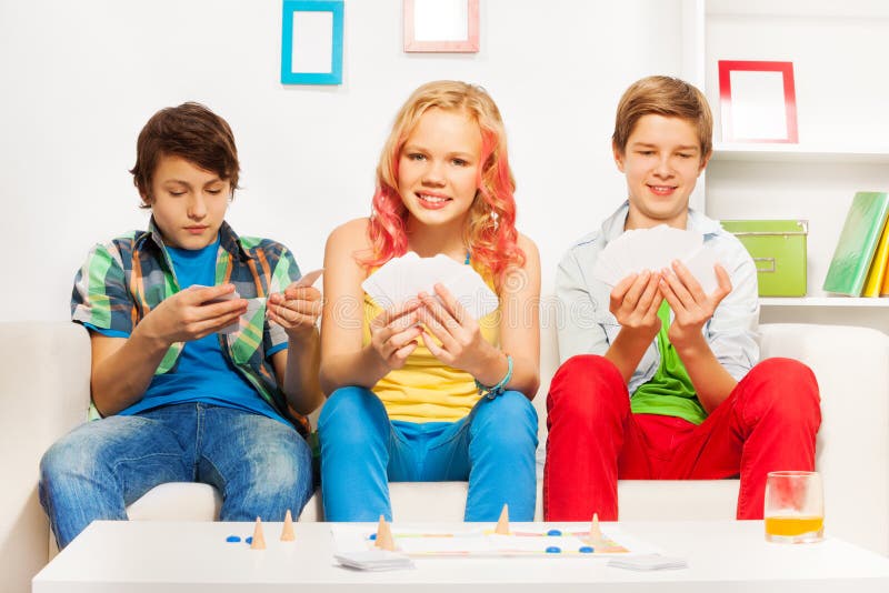 Three teenagers playing table game on white sofa