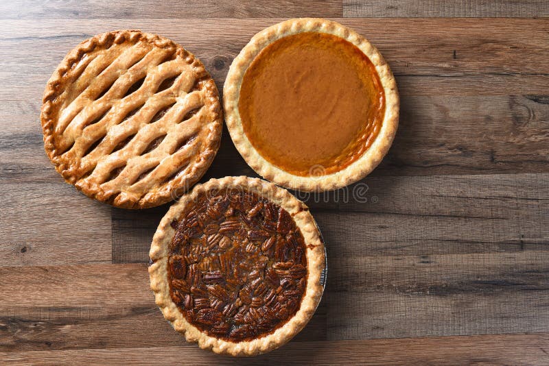 Three pies for Thanksgiving on a wood surface. The desserts include apple, pumpkin and pecan pies - all traditional treats for the American Holiday. Three pies for Thanksgiving on a wood surface. The desserts include apple, pumpkin and pecan pies - all traditional treats for the American Holiday.