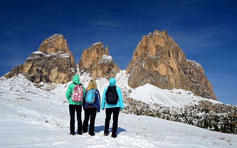 Three tourists looking at the beautiful mountain group Sassolungo Langkofel. Beautiful snowy winter landscape in Dolomites. Province of Trento, South Tyrol, Italy.