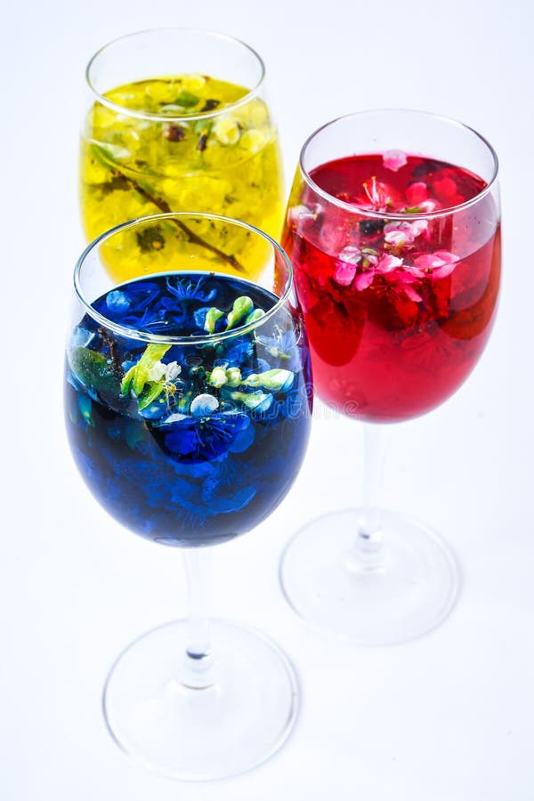 Three wine glasses of spring blossom flowers, with yellow, red and blue water on white background, bar and spring time cocktails