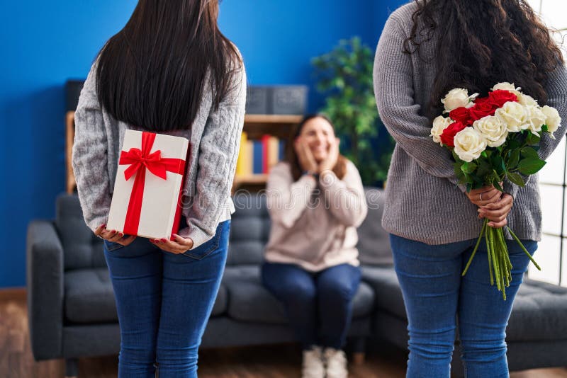 Three Woman Surprise with Gift and Flowers on Back at Home Stock Photo